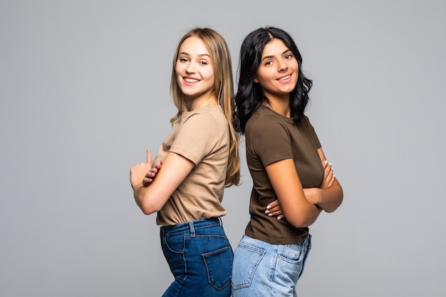 Dos mujeres jóvenes de pie espalda con espalda contra la pared blanca.