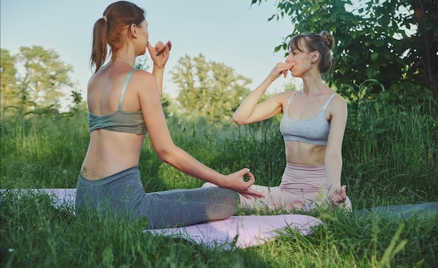 Dos mujeres jóvenes practicando la respiración y haciendo yoga al aire libre