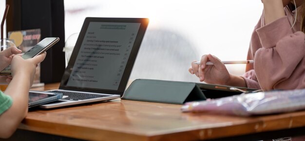 Dos mujeres jóvenes que usan una computadora portátil y una tableta digital estudiante universitaria haciendo uso de la computadora para aprender en línea con su amiga en el café