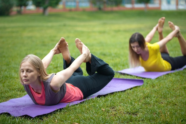 Dos mujeres jóvenes realizan entrenamiento para la flexibilidad en el parque, disparo de teleobjetivo