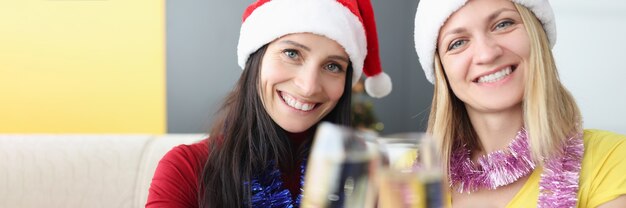 Dos mujeres jóvenes con sombreros de santa claus bebiendo champán