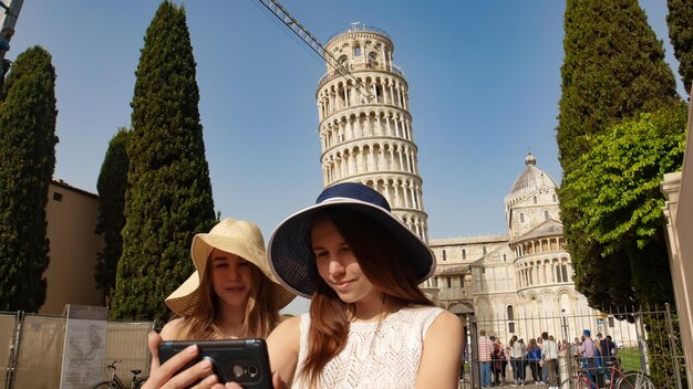 Dos mujeres jóvenes toman un selfie bajo la torre inclinada de Pisa