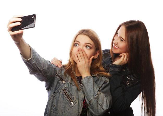 Foto dos mujeres jóvenes tomando selfies con teléfonos móviles aislados en blanco