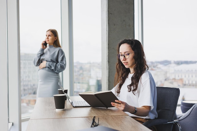 Dos mujeres jóvenes trabajan en una oficina moderna Espacio de oficina de trabajo con grandes ventanas Mujer gerente trabaja en el escritorio sentada en la oficina