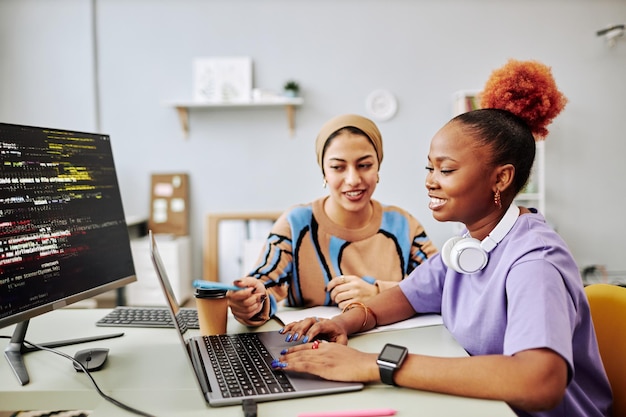 Dos mujeres jóvenes trabajando juntas en un proyecto de desarrollo de software y sonriendo