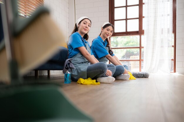 Dos mujeres jóvenes en uniforme limpiando la habitación mientras están sentadas en el suelo