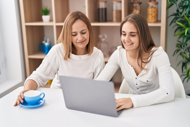 Dos mujeres madre e hija usando laptop tomando café en casa