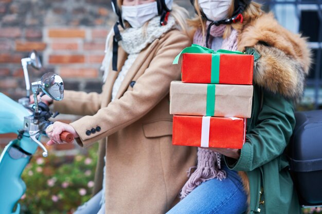 Dos mujeres con máscaras y sosteniendo bolsas de la compra viajando en scooter