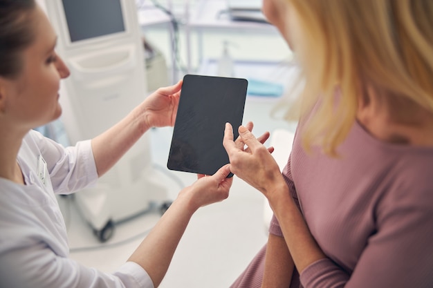 Dos mujeres mirando la pantalla de la tableta mientras se discute el procedimiento de belleza de elevación