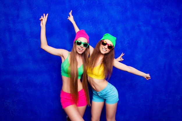 Dos mujeres de moda con sombreros y espectáculos bailando en azul