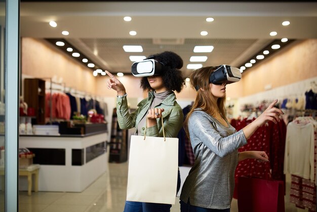 Dos mujeres con modernos auriculares de realidad virtual que tienen experiencia en compras en una tienda de lencería