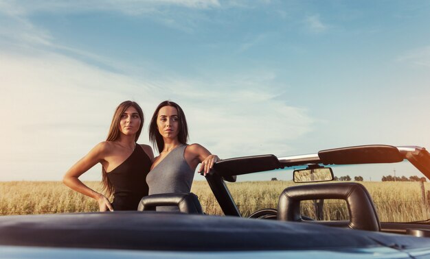 Dos mujeres morenas de pie cerca de su auto