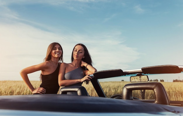 Dos mujeres morenas sexy de pie cerca de su coche