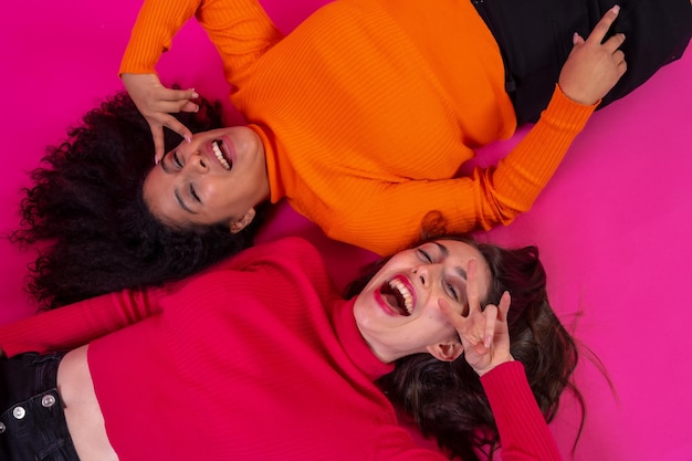 Dos mujeres multiétnicas acostadas sonriendo en una pose de moda en un estilo de vida de fondo rosa