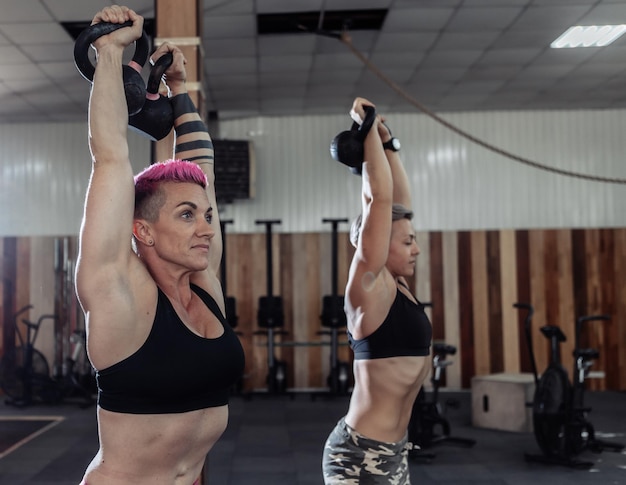 Dos mujeres musculosas y poderosas están haciendo ejercicio con pesadas pesas rusas. Entrenamiento atletico. Entrenamiento cruzado y funcional en un gimnasio moderno