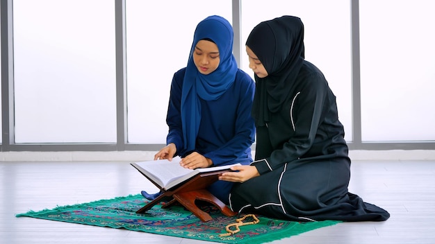 Dos mujeres musulmanas asiáticas que llevan el hijab tradicional están recitando oraciones en el Corán