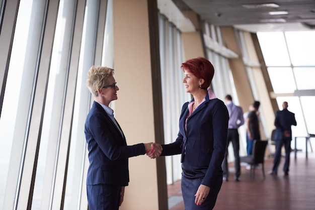 dos mujeres de negocios corporativos en el moderno y luminoso interior de la oficina hacen un trato y un apretón de manos