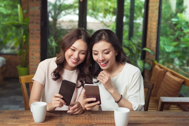 Dos mujeres de negocios jóvenes sentados a la mesa en la cafetería. Chica muestra la imagen de su amiga en la pantalla del teléfono inteligente