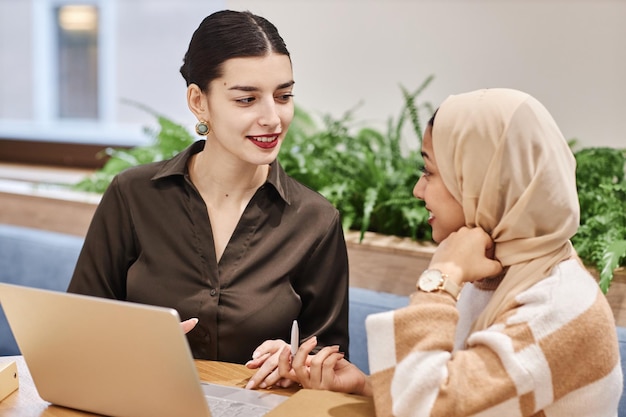 Dos mujeres de negocios de Oriente Medio usando una computadora portátil juntas en la oficina