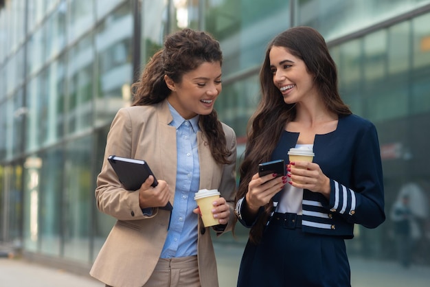 Dos mujeres de negocios sosteniendo una taza de café y mirando el teléfono