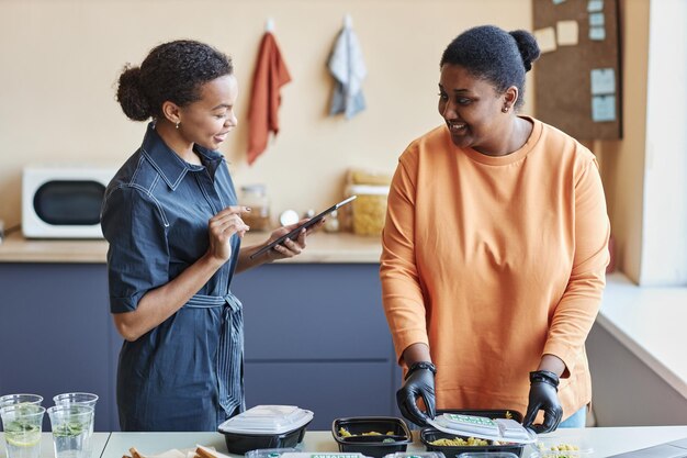 Dos mujeres negras revisando pedidos de comida a domicilio en una cafetería y usando una tableta