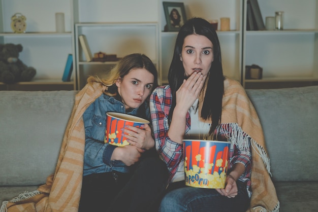 Foto las dos mujeres con palomitas de maíz ven una película de terror en el sofá