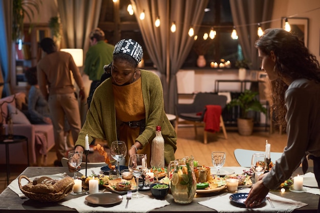 Dos mujeres poniendo la mesa del comedor para una cena festiva con sus amigos en la sala de estar