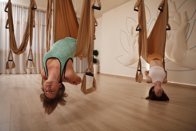 Dos mujeres practicando yoga antigravedad en una hamaca de yoga aérea en un estudio deportivo