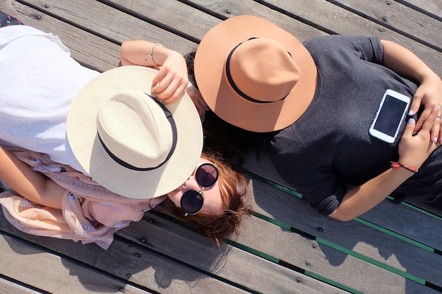 Dos mujeres relajadas y sombrero. Acuéstese en un puente de madera que se extiende hasta el mar.