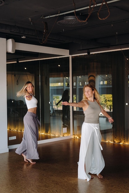 Dos mujeres en ropa deportiva están haciendo danza yoga en el gimnasio.