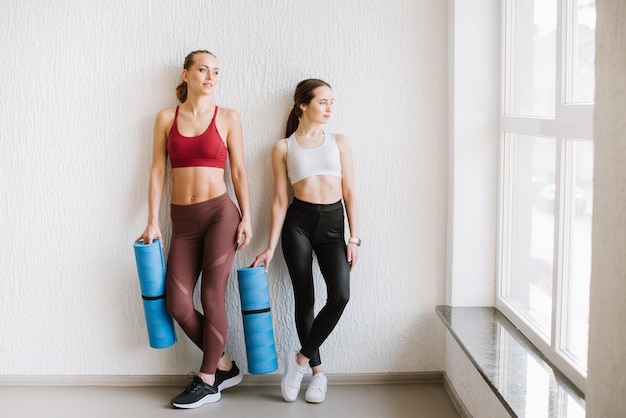 Dos mujeres en ropa deportiva posando con equipos de fitness en el gimnasio.