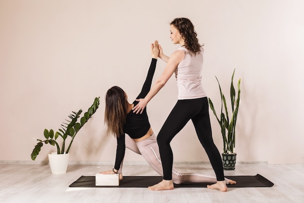 Dos mujeres en ropa deportiva practicando yoga haciendo una estocada baja sobre una pierna con un giro o Anjanasana o Anjaneyasana Crescent Pose o Young Moon Pose