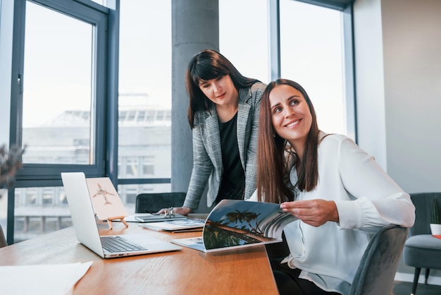 Dos mujeres con ropa formal están adentro en la oficina moderna trabajando juntas