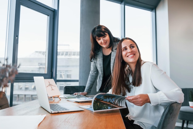 Dos mujeres con ropa formal están adentro en la oficina moderna trabajando juntas