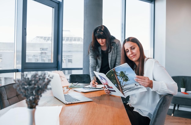 Dos mujeres con ropa formal están adentro en la oficina moderna trabajando juntas