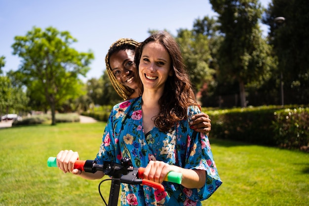 Dos mujeres con un scooter eléctrico junto a un jardín.