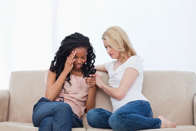 Dos mujeres sentadas en un sofá están mirando un teléfono móvil