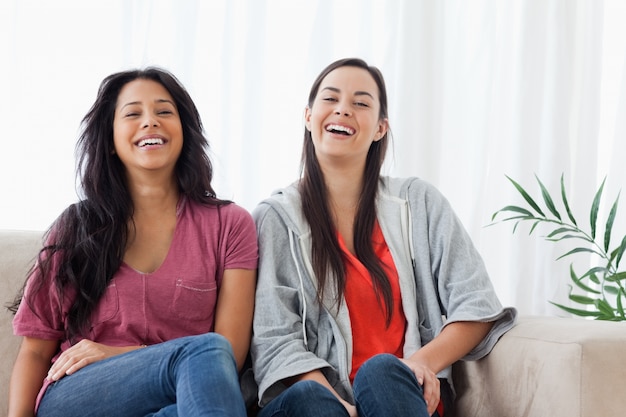Dos mujeres se sientan al lado de otra en el sofá mientras se ríen
