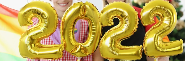 Dos mujeres con sombrero de santa sosteniendo globos de helio con números en el fondo de la bandera lgbt y