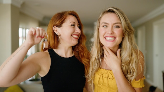 Dos mujeres sonriendo confiadas sosteniendo la llave del nuevo hogar en casa