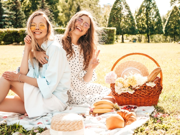 Dos mujeres sonrientes hermosas jóvenes en vestido de verano de moda y sombreros. Mujeres despreocupadas haciendo picnic al aire libre.