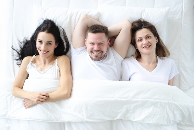 Dos mujeres sonrientes y un hombre yacen en la cama