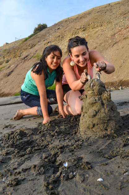 Dos mujeres sonrientes posan junto a una muñeca de tierra que montaron a la orilla del mar