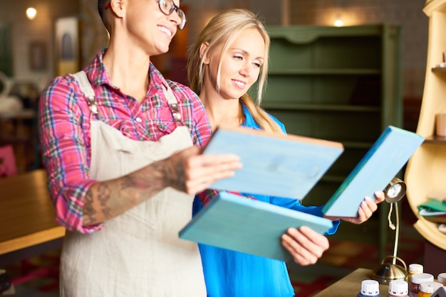 Dos mujeres sonrientes que eligen cuadros para la decoración interior