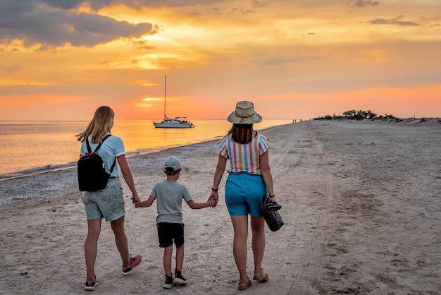 Dos mujeres toman las manos de un hijo Vacaciones en familia en la costa del mar. Precioso atardecer