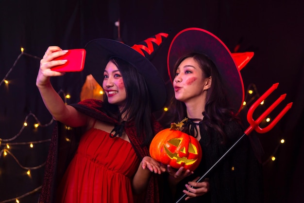 Foto dos mujeres tomando fotos con su teléfono móvil en una fiesta de halloween. selfie con un teléfono móvil en la fiesta.