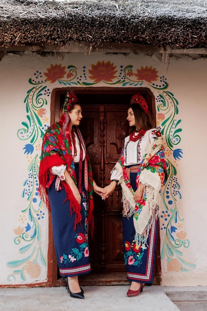 Dos mujeres ucranianas vestidas con ropa étnica tradicional y una corona floral roja en el fondo de una choza decorada Vestido bordado nacional ucraniano llamada vyshyvanka Ore por Ucrania