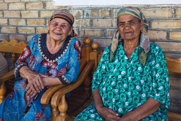 Dos mujeres uzbekas con ropas tradicionales están sentadas en un banco de madera