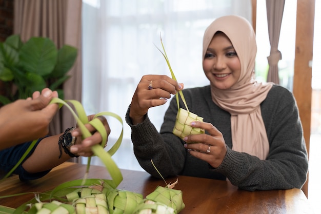 Dos mujeres con velo hacen una envoltura tejida de ketupat