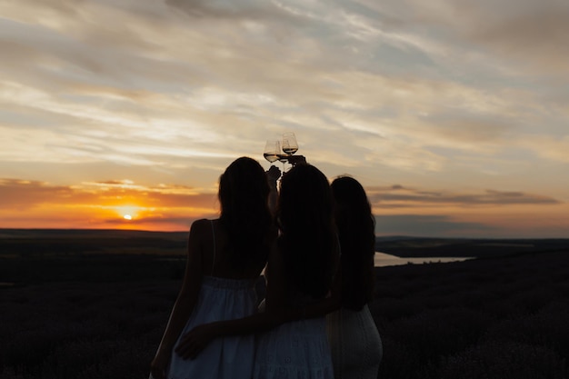 Dos mujeres vestidas de blanco sostienen una copa de vino al atardecer.